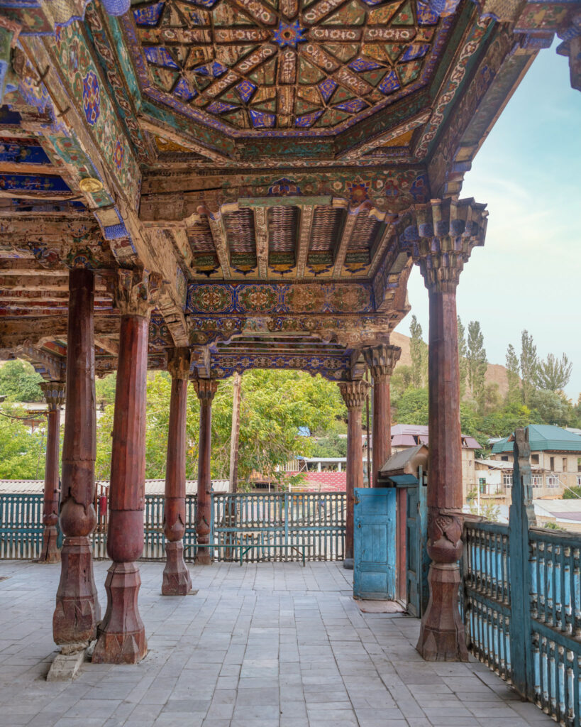 Avancée à colonnes de bois sculpté et plafond peint d’une mosquée traditionnelle d’Asie centrale.