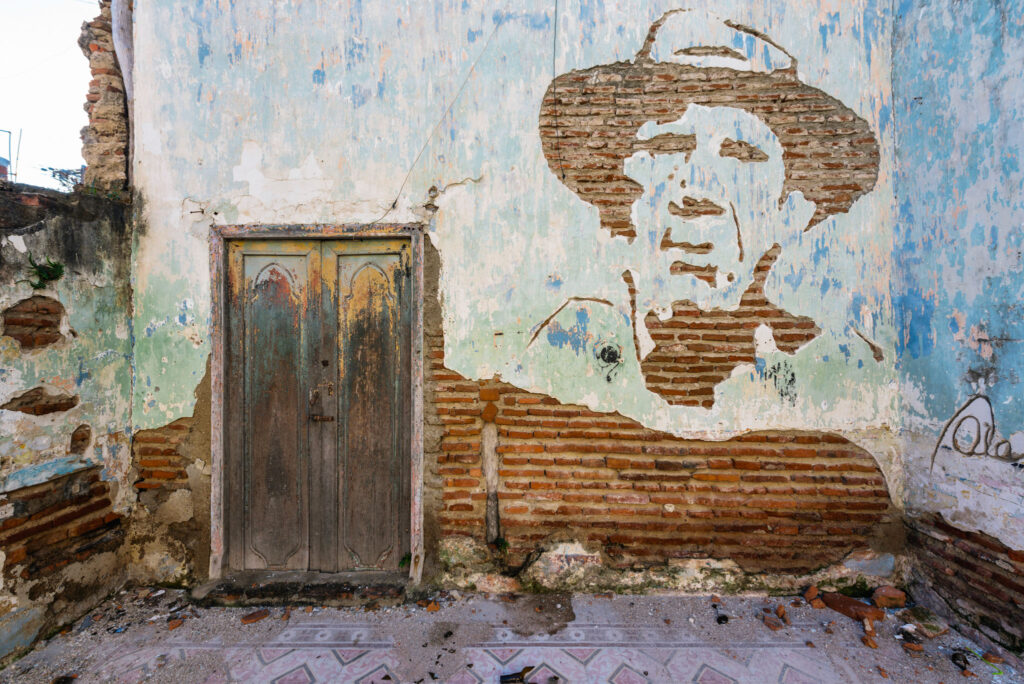 Portrait de Camilo Cienfuegos gravé dans le crépi d’un mur en ruine où les briques apparentes forment le dessin.