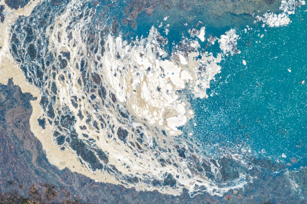 Abstraction visuelle et textures d'écume de mer mêlée aux sédiments côtiers sur le littoral breton.