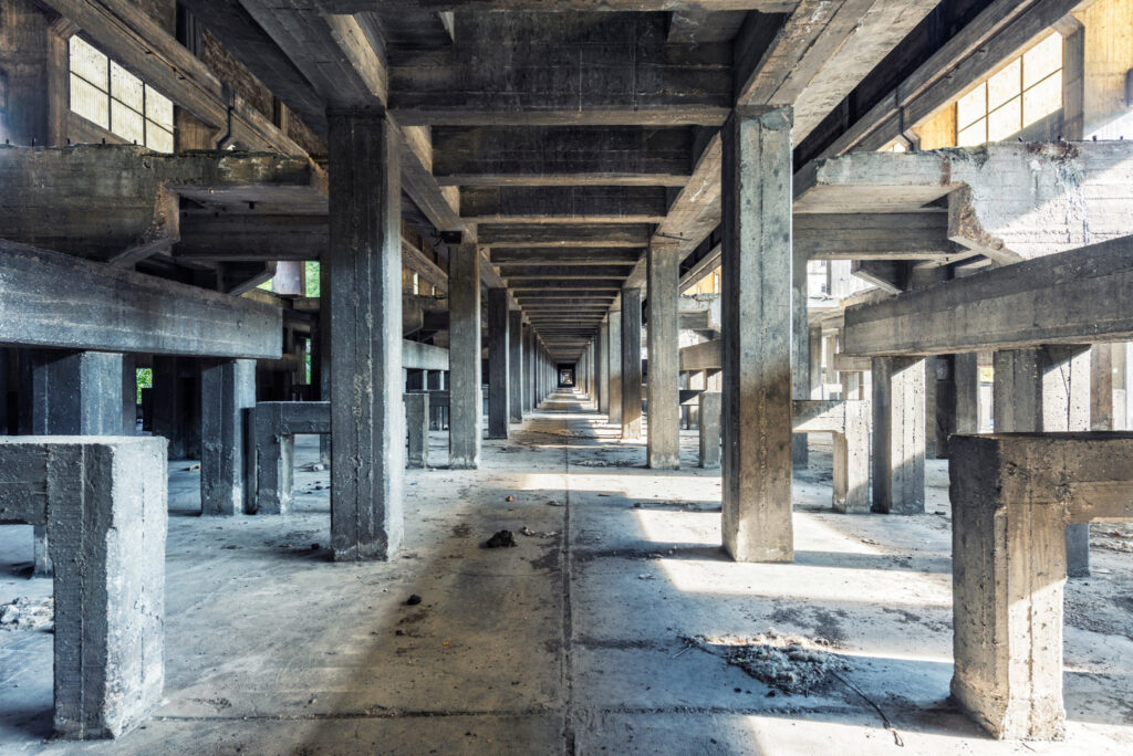 ALT Vaste halle en béton d’une ancienne usine italienne de production d’aluminium, rythmée par des piliers massifs et des fenêtres latérales.