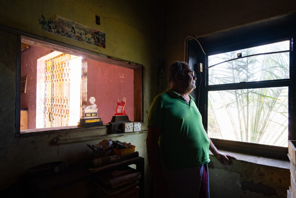 Homme debout dans un ancien cinéma au Sri Lanka, près d’un guichet où sont exposés des trophées.