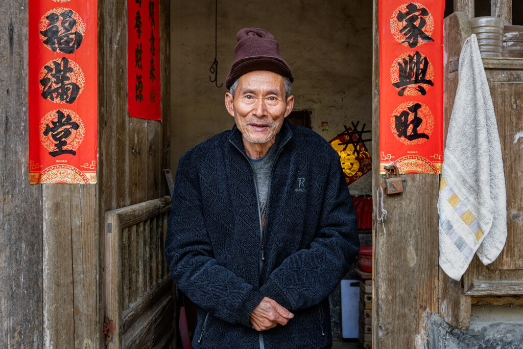 Portrait d’un homme devant l’entrée d’une maison traditionnelle dans un village presque abandonné du Fujian, en Chine.