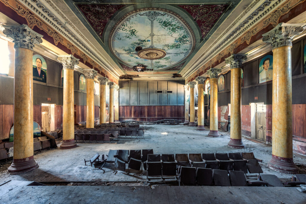 Théâtre soviétique abandonné dans la maison de la culture d’Ochkhamuri en Adjarie, avec colonnes, lustre, portraits communistes et rangées de sièges.