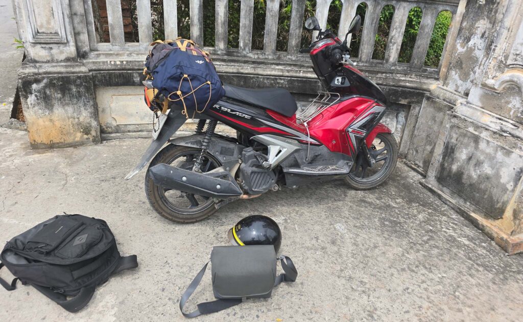 Sac photo, trépied, drone et équipement de voyage posés près d’un scooter dans un bâtiment au Vietnam.
