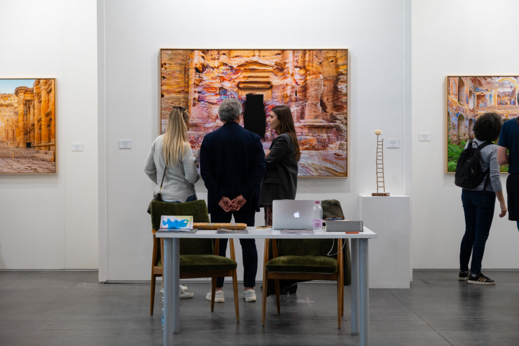 Visiteurs sur le stand de la Camilla Prini Gallery devant une photographie grand format de Pétra réalisée par Aurélien Villette
