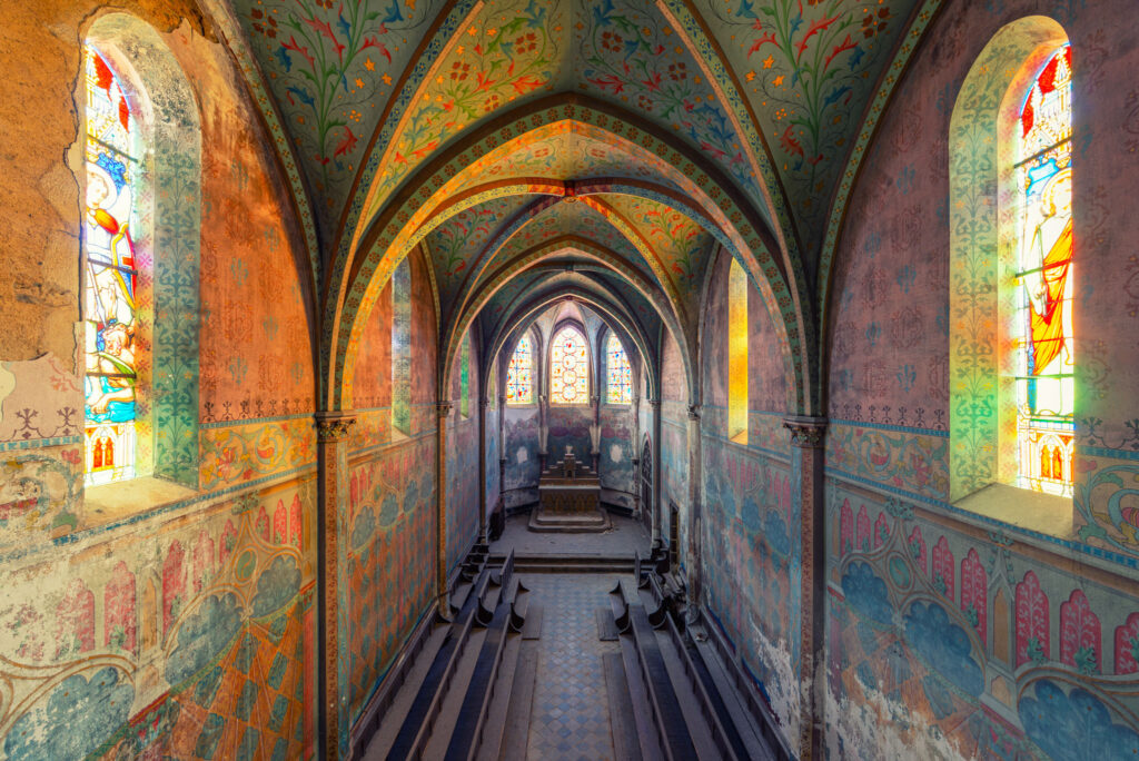 Intérieur de la chapelle néogothique de l’ancien collège de Lourdoueix-Saint-Michel, avec voûte peinte de motifs végétaux, fresques murales et vitraux.