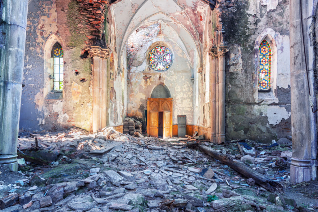 Nef en ruine de la chapelle d’un ancien pensionnat dans l’Hérault, avec charpente effondrée, gravats et rosace au-dessus de la porte