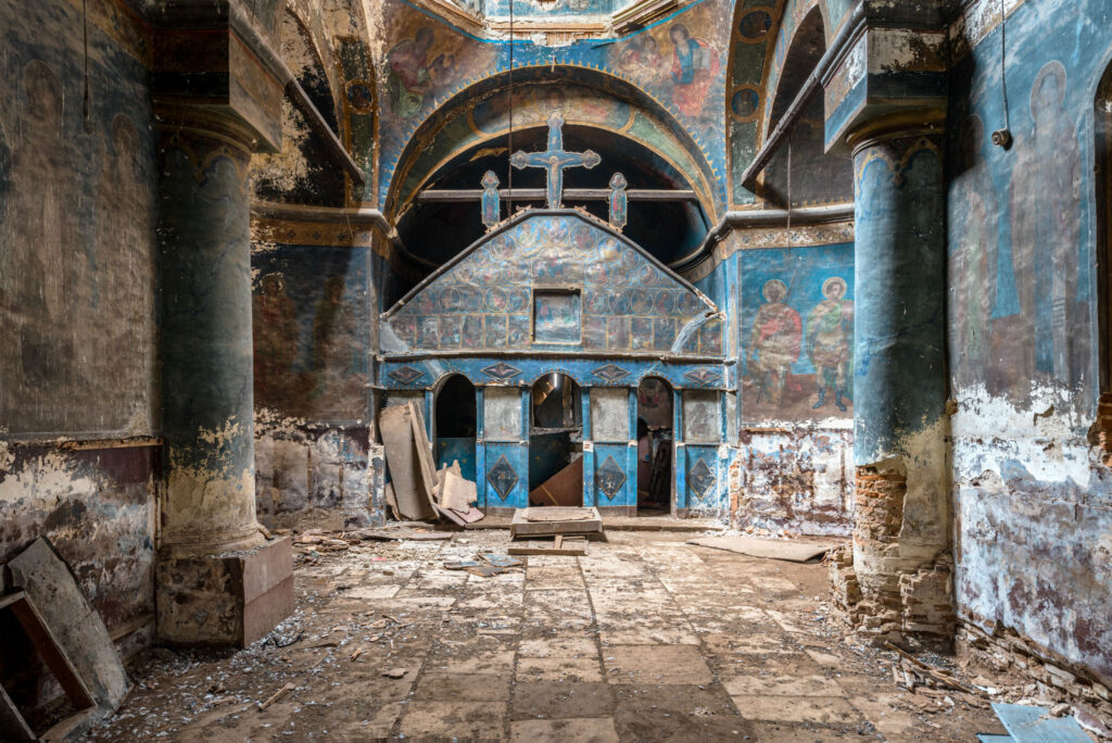 Intérieur d’une église orthodoxe abandonnée près de Bucarest, avec colonnes massives, peintures murales et iconostase bleue surmontée de croix