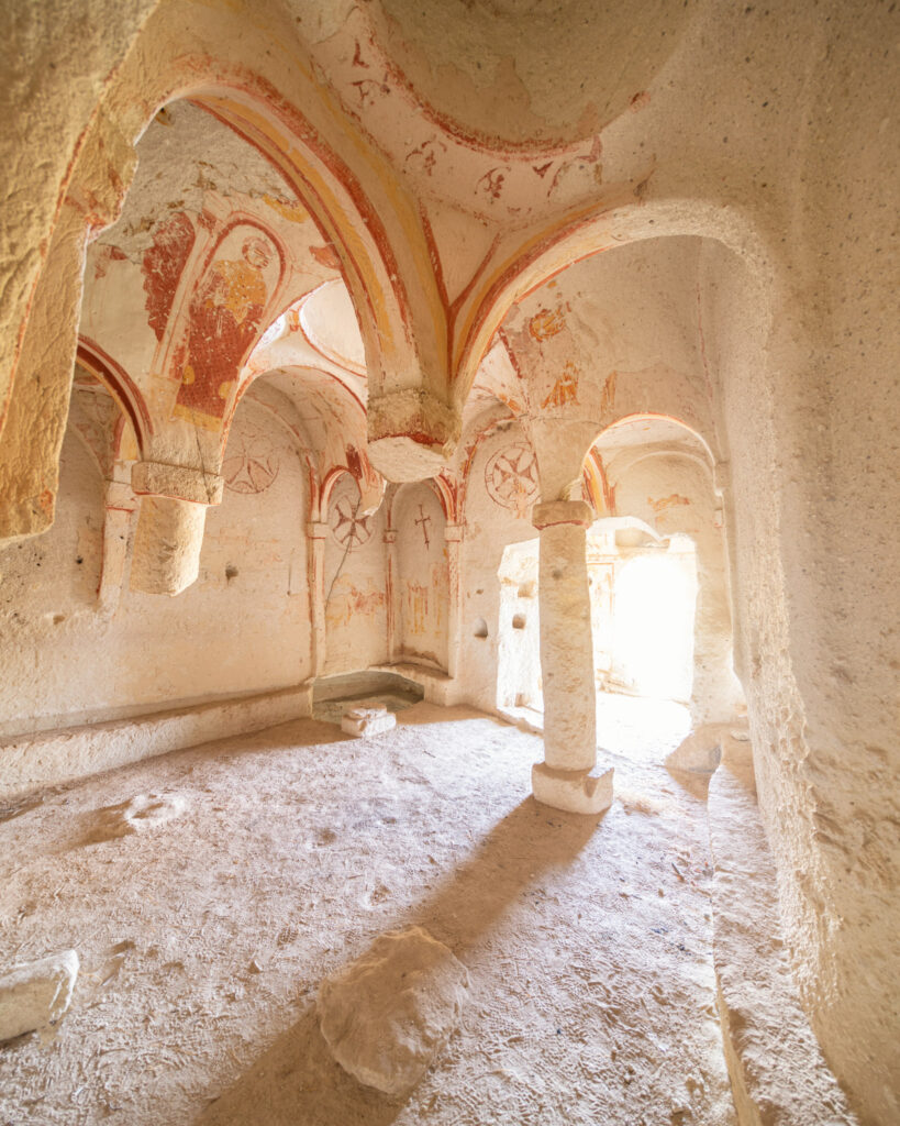Intérieur d’une église rupestre de Cappadoce creusée dans le tuf volcanique, avec piliers sculptés dans la roche et croix rouges peintes sur les parois.