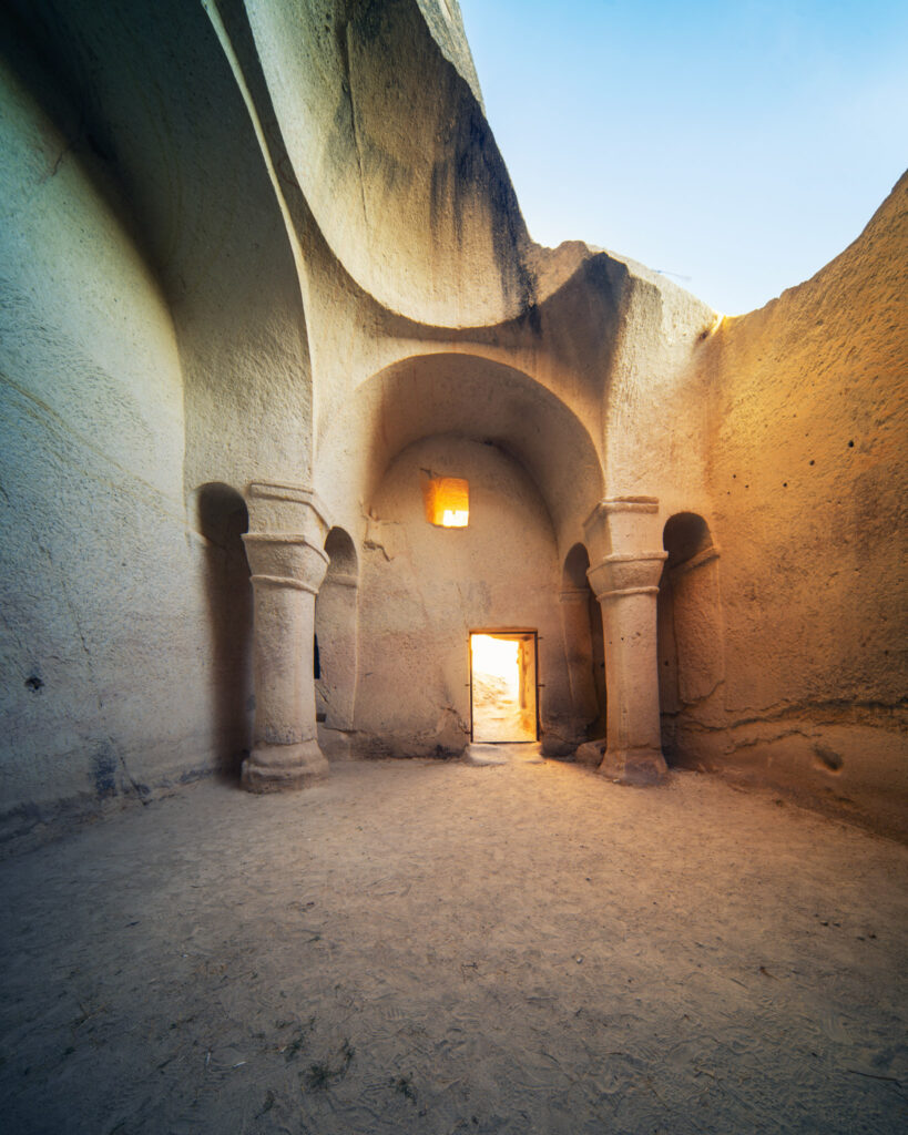 Intérieur d’une ancienne église troglodyte de Cappadoce, avec colonnes sculptées dans la roche, arches taillées dans le tuf et ouverture devenu naturelle vers le ciel.