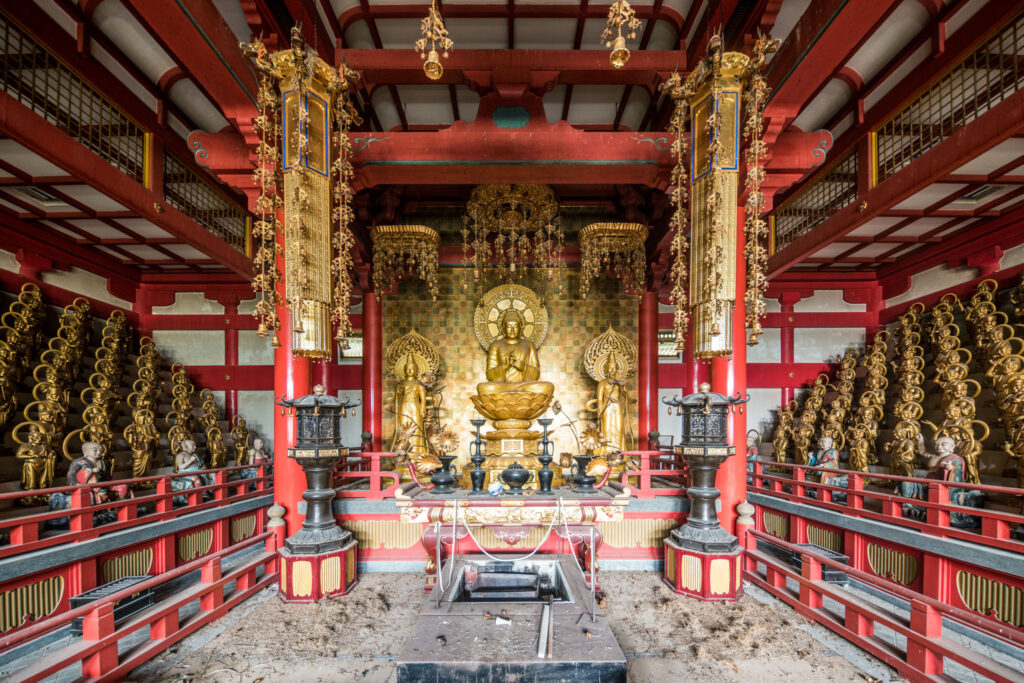Salle bouddhique abandonnée de Saikai Rakuen au Japon, avec un Bouddha doré entouré de centaines de statues d’arhats alignées.