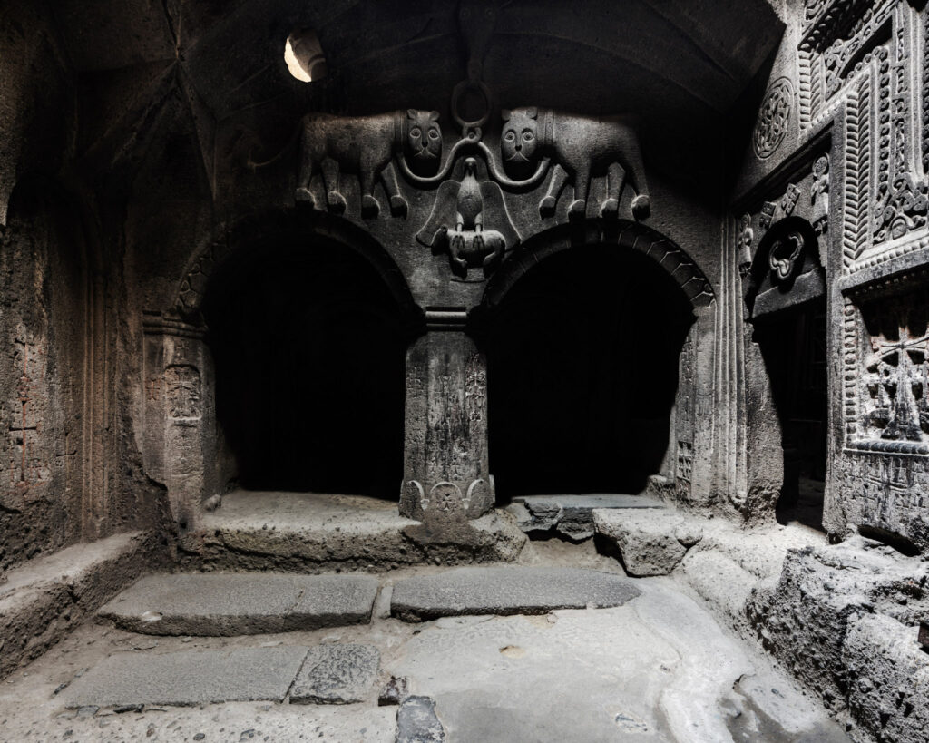 Chapelle rupestre du monastère de Geghard, avec arches sculptées, colonnes de pierre et ouvertures laissant entrer une faible lumière