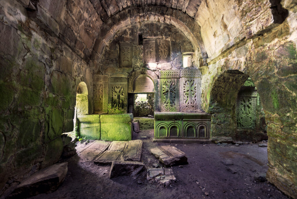 Salle voûtée en pierre du monastère de Matosavank, avec ancien mobilier liturgique vert, murs couverts de mousse et sol encombré de débris