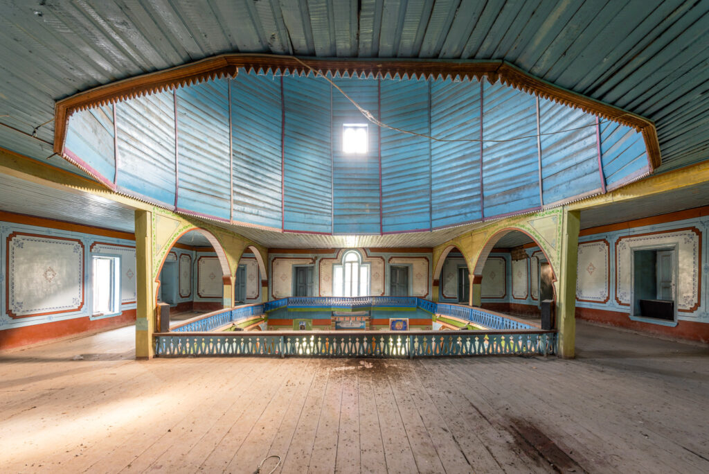 Intérieur d’une mosquée traditionnelle en bois d’Azerbaïdjan, avec structure octogonale sculptée, galerie supérieure et plafond peint en bleu.