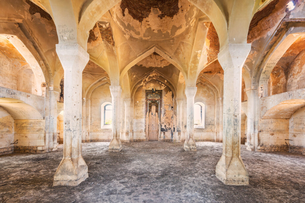 Salle de prière endommagée de la mosquée Juma d’Ağdam, rythmée par des colonnes blanches et des voûtes aux enduits lacunaires