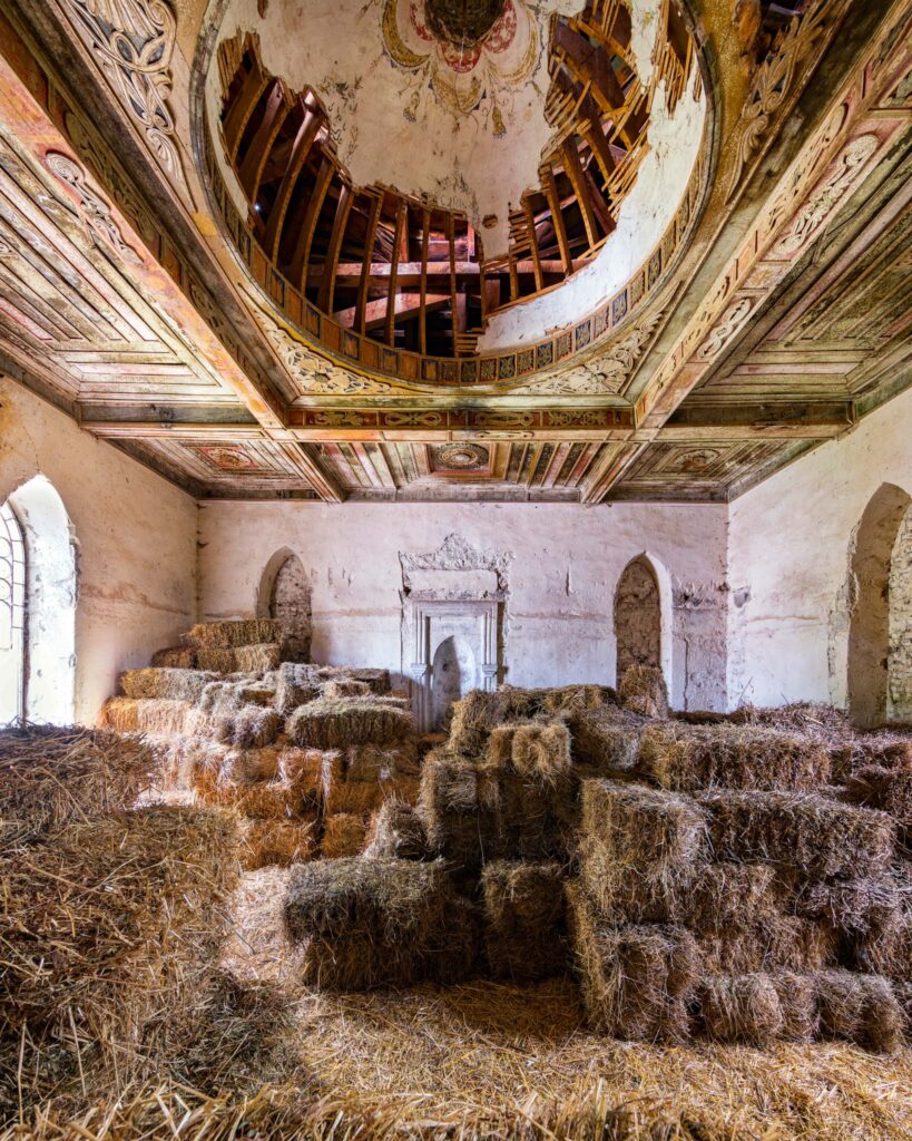 Intérieur d’une ancienne mosquée meskhète en Géorgie, rempli de bottes de foin témoignant de l’activité locale, sous une coupole en bois peinte et partiellement effondrée.