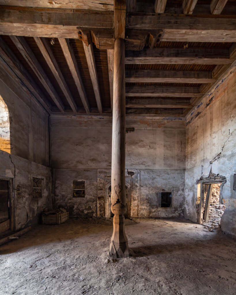 Intérieur d’une mosquée en cours de restauration à Boukhara, avec charpente apparente, murs bruts et pilier central en bois sculpté