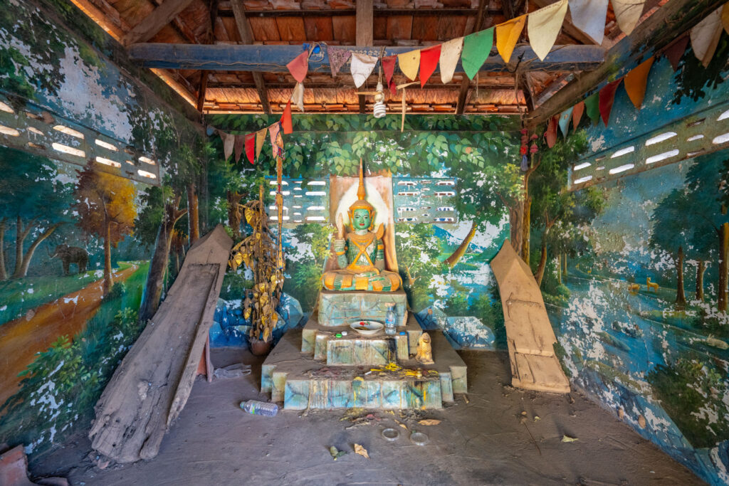 Sanctuaire bouddhique cambodgien avec statue verte d’un Bouddha assis, peintures murales colorées et décorations suspendues.