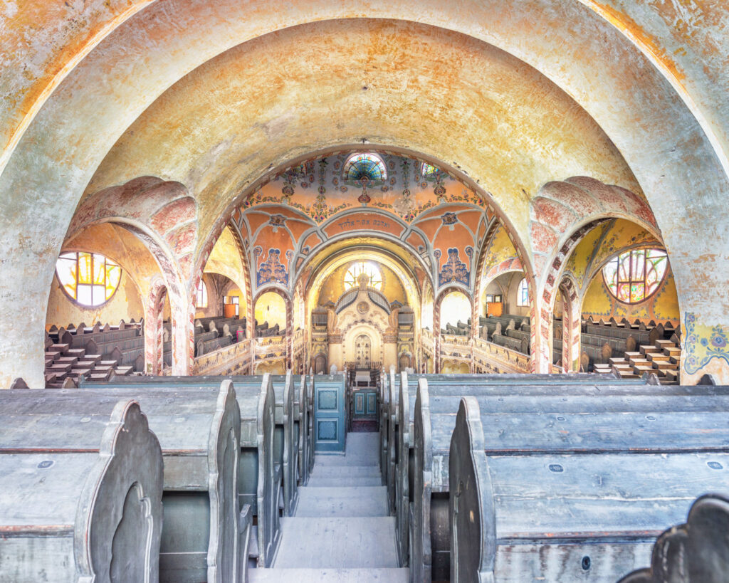 Intérieur de la synagogue de Subotica avant restauration, avec coupole Art nouveau, décors floraux polychromes et bancs abandonnés.