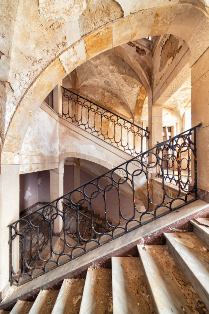 Escalier à jour central avec rampe métallique dans une ancienne prison de Sicile, révélant la structure verticale du bâtiment.