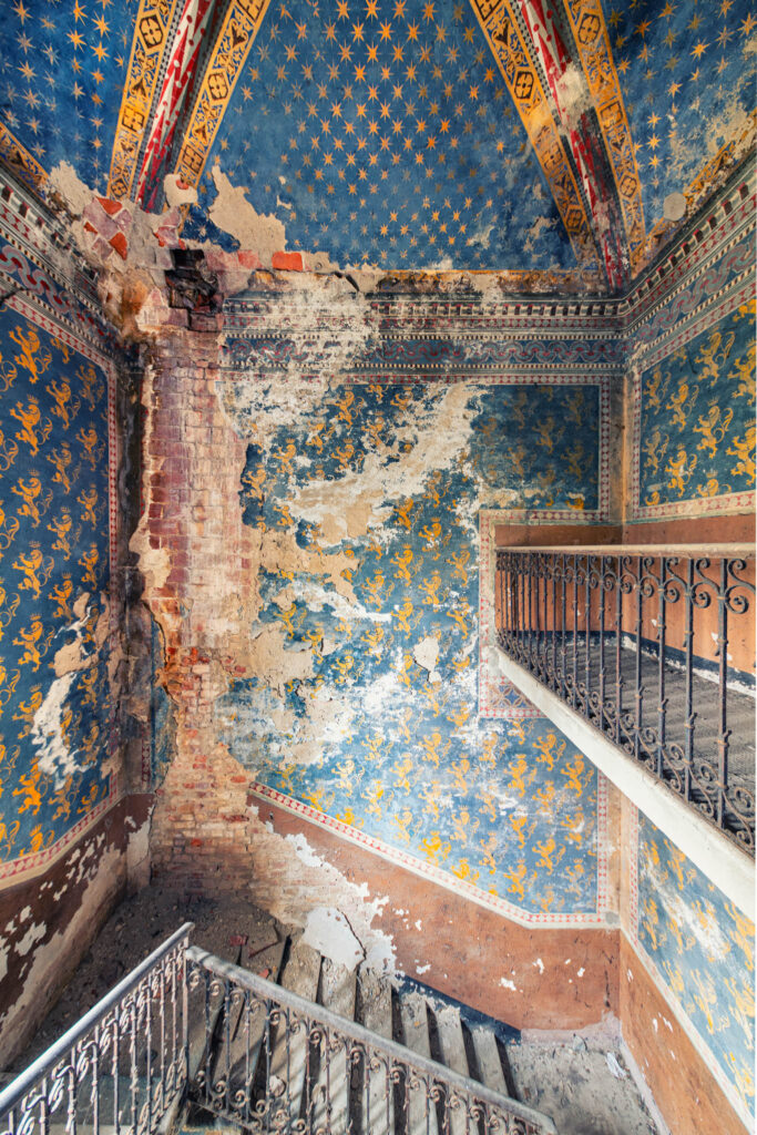 Escalier principal décoré de peintures murales bleues et d’un écusson dans une ancienne cascina italienne.