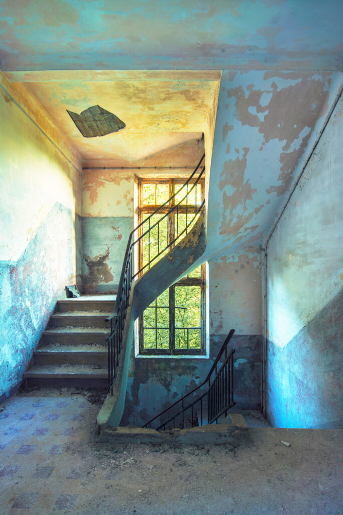 Escalier utilitaire d’une ancienne caserne militaire française avec peinture murale à mi-hauteur et lumière naturelle colorée.