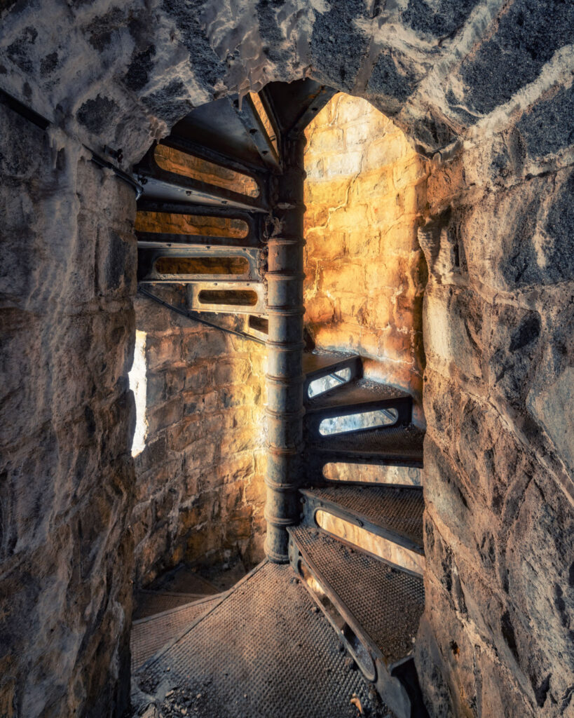 Escalier métallique dans le pilier d’un ancien pont de type Eiffel abandonné, éclairé par une lumière hivernale.