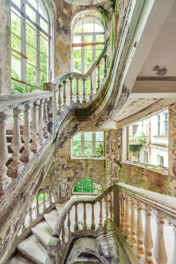 Grand escalier courbe d’un sanatorium abandonné de Gagra, entouré de fenêtres brisées et de végétation