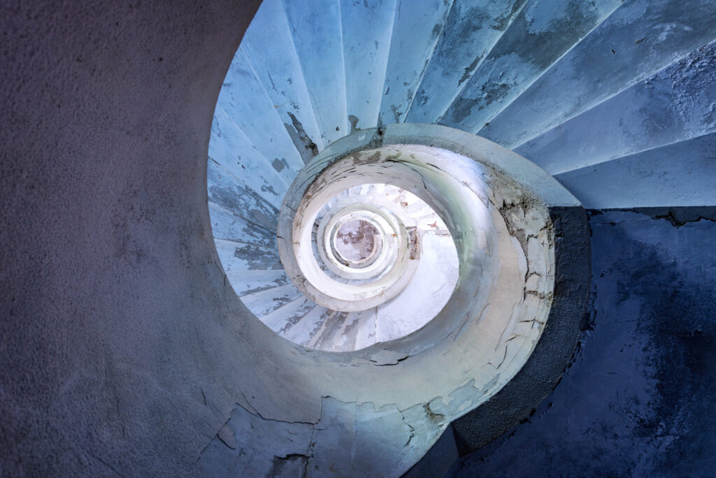 Escalier secondaire éclairé par deux petites fenêtres dans un ancien sanatorium italien.