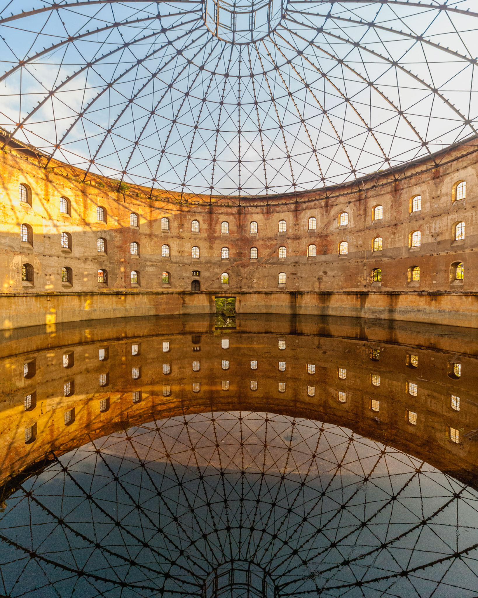 Intérieur circulaire en brique du Gasometer Nord à Leipzig, avec charpente métallique et reflets au sol.