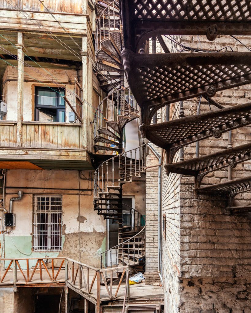 Cour intérieure pavée dans un ancien quartier de Tbilisi, avec façades patinées, escaliers en fer forgés