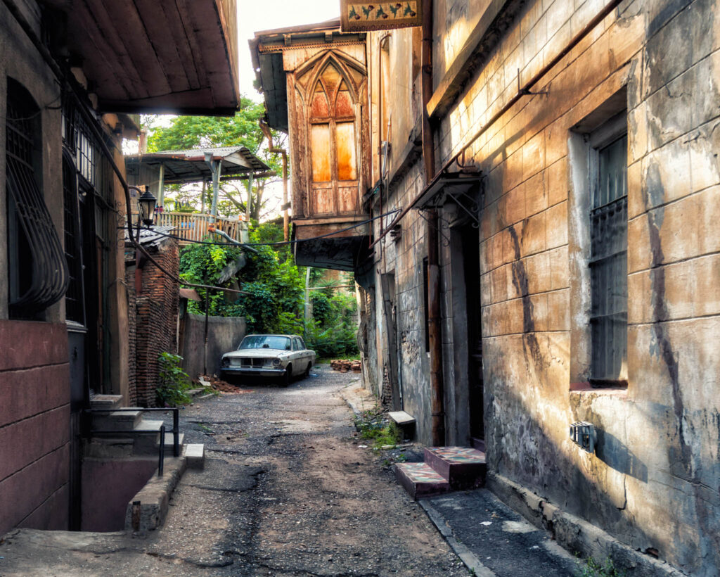 Façade ancienne de Tbilisi envahie par la végétation, avec fenêtres en bois, voiture abandonée