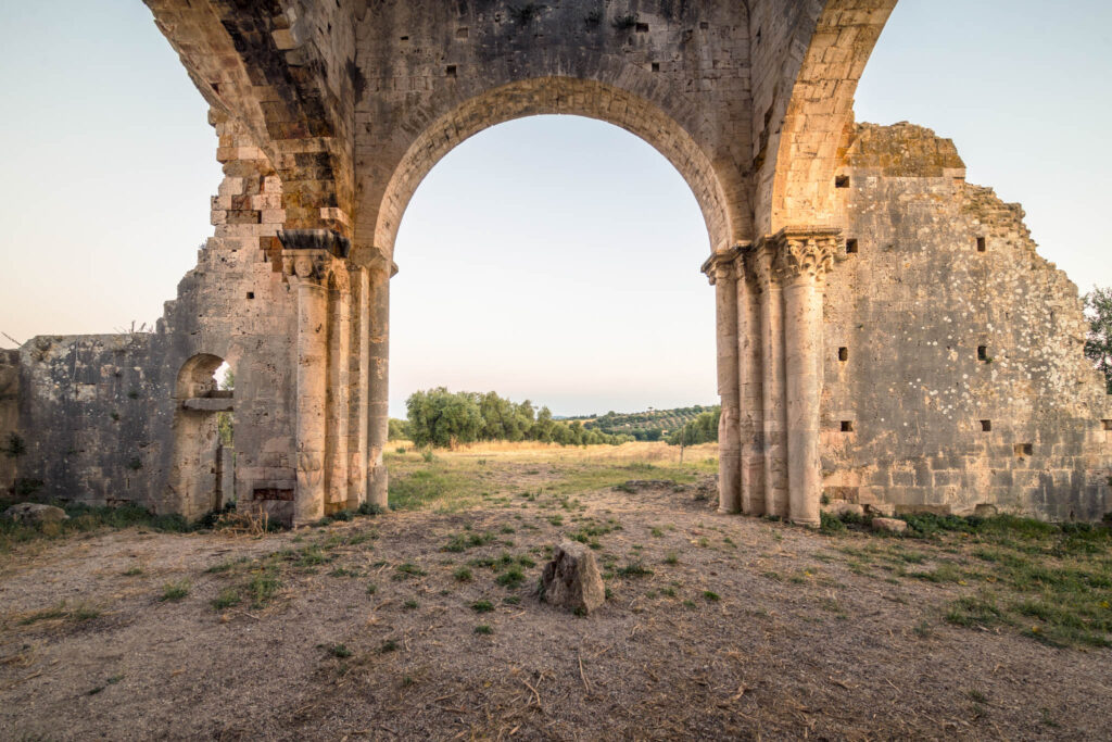 Grande arche en pierre d’une ancienne abbaye romane en ruine, entourée d’oliviers dans la campagne toscane aux premières lueurs du matin