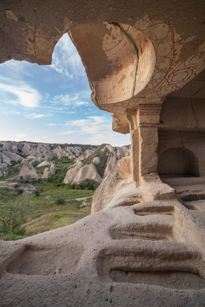 Intérieur troglodytique creusé dans le tuf volcanique de Cappadoce avec colonne sculptée, ouverture sur la vallée et cavités dans le sol