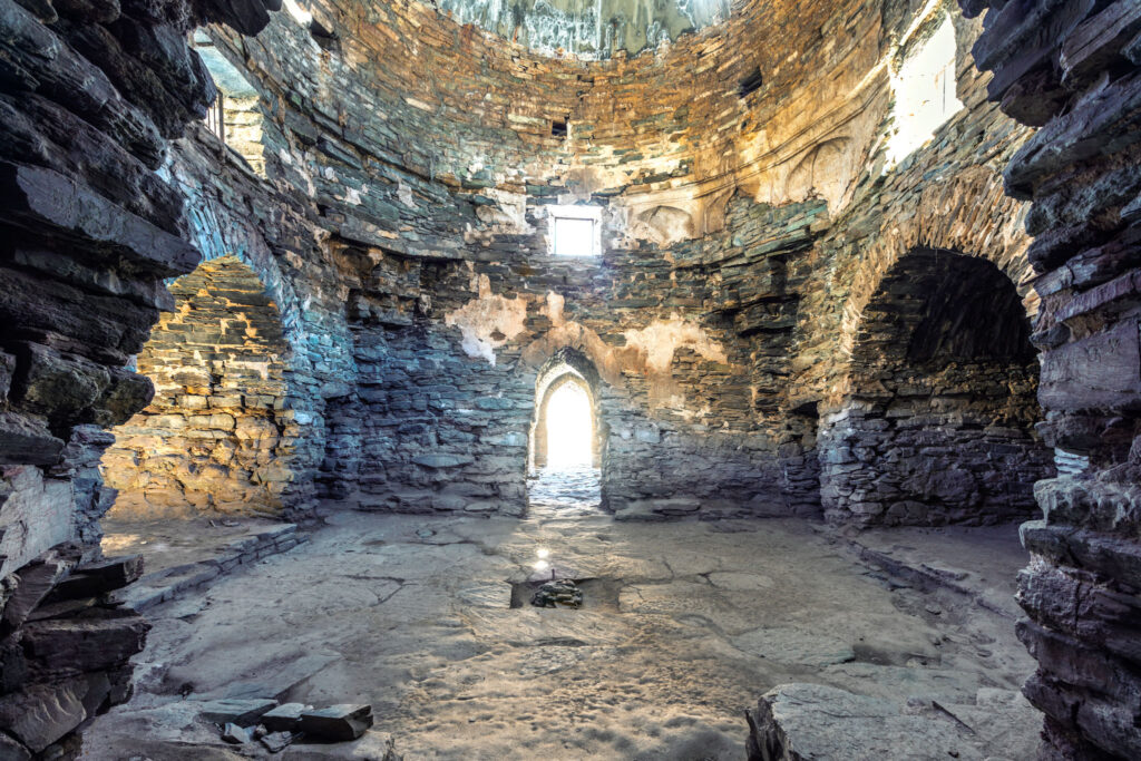 Salle sombre en pierre du caravansérail de Tash Rabat avec voûte, ouverture étroite et lumière traversant l’architecture médiévale