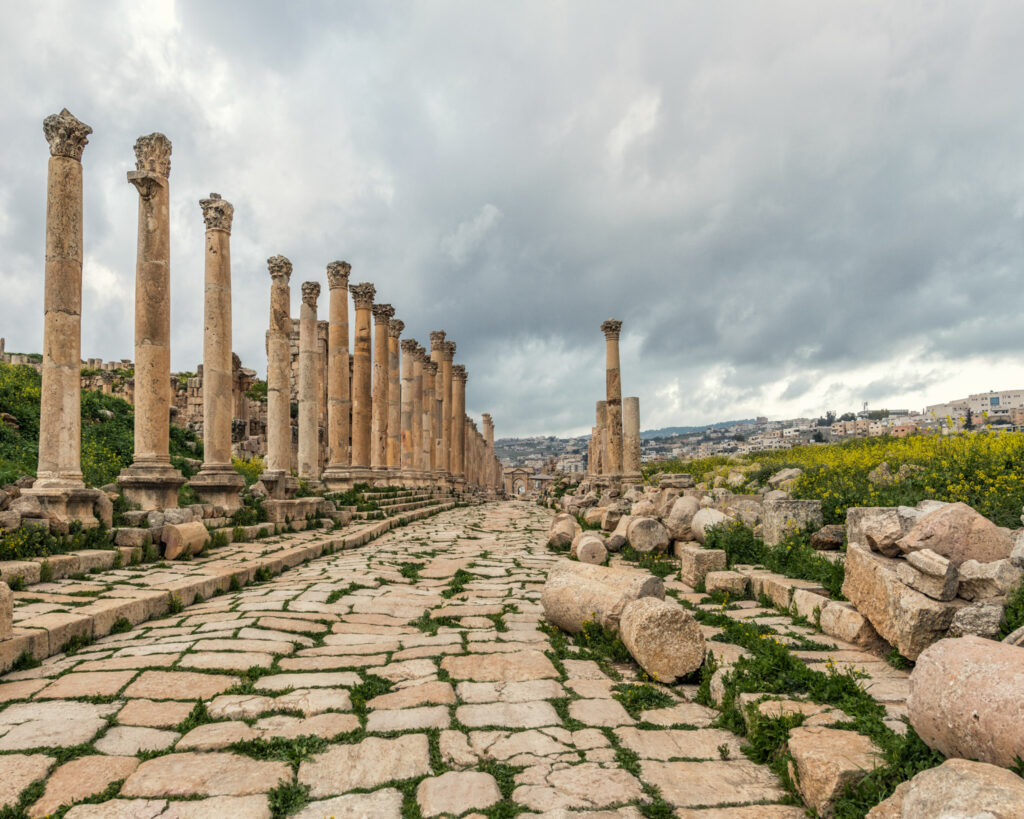 Rue romaine pavée du Cardo Maximus de Jerash, bordée de colonnes en calcaire local sous un ciel nuageux en Jordan