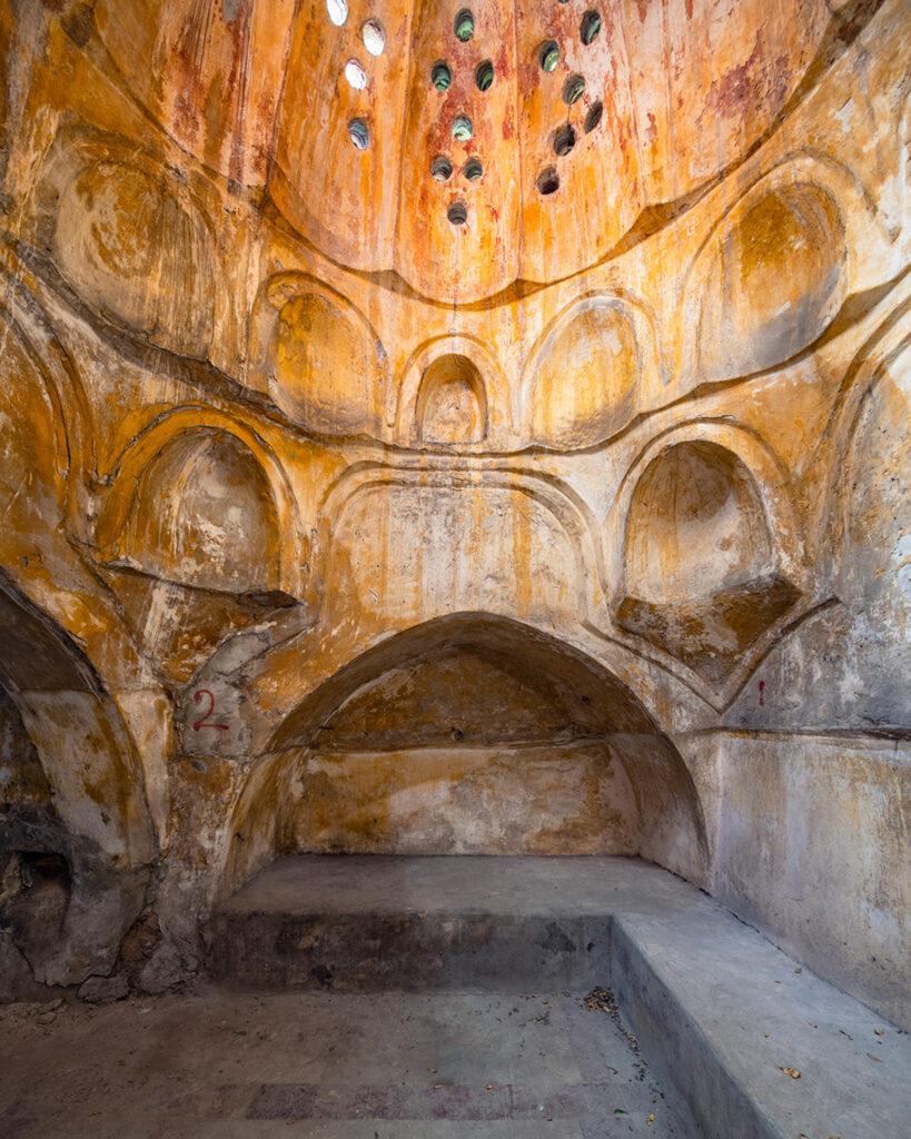 Salle voûtée du hammam mamelouk Al-Nouri à Tripoli avec niches murales, enduits ocre et ouvertures colorées laissant entrer la lumière