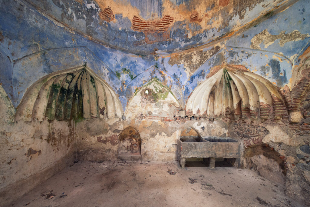 Intérieur abandonné d’un hammam de tradition ottomane avec coupoles, alcôves arrondies et anciens enduits bleus écaillés