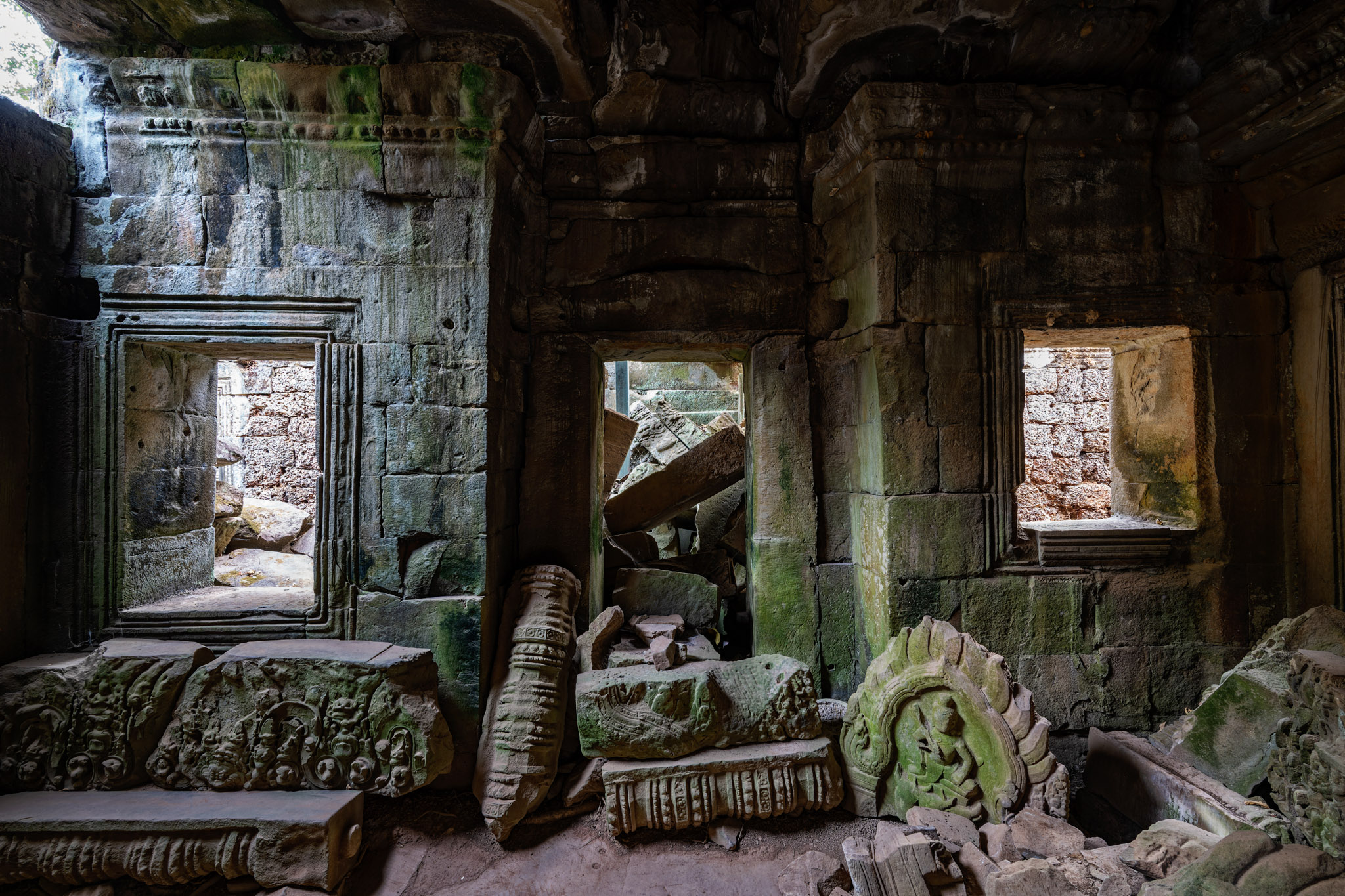 Intérieur sombre du temple khmer de Ta Prohm avec portes sculptées, blocs de pierre effondrés et végétation après le coucher du soleil