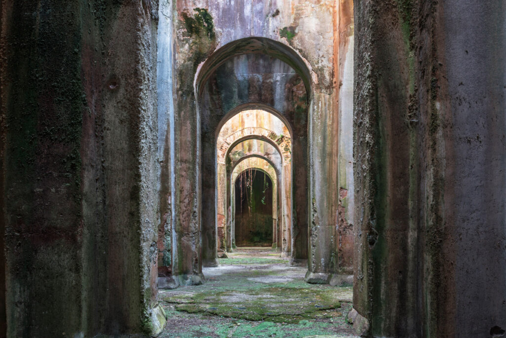 Galerie souterraine de la Piscina Mirabilis en Campanie avec rangées de piliers, voûtes en berceau et faisceau de lumière zénithale
