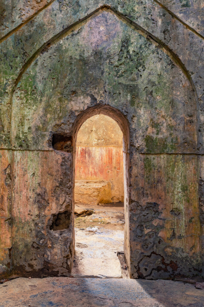 Porte en arc brisé entre deux salles d’un ancien hammam turc, entourée d’enduits patinés verts, bleus, roses et ocre