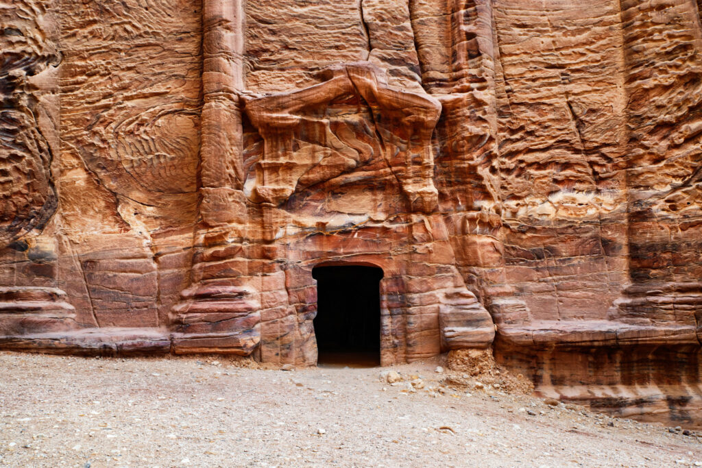 Porte sombre d’une tombe rupestre de Pétra creusée dans un grès naturellement veiné d’ocre, de rouge, de rose et de violet