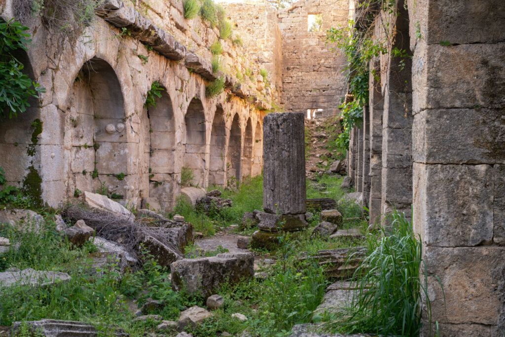 Portique d’une cité antique de Pamphylie avec colonnes et murs de pierre dispersés dans une végétation dense en Turquie