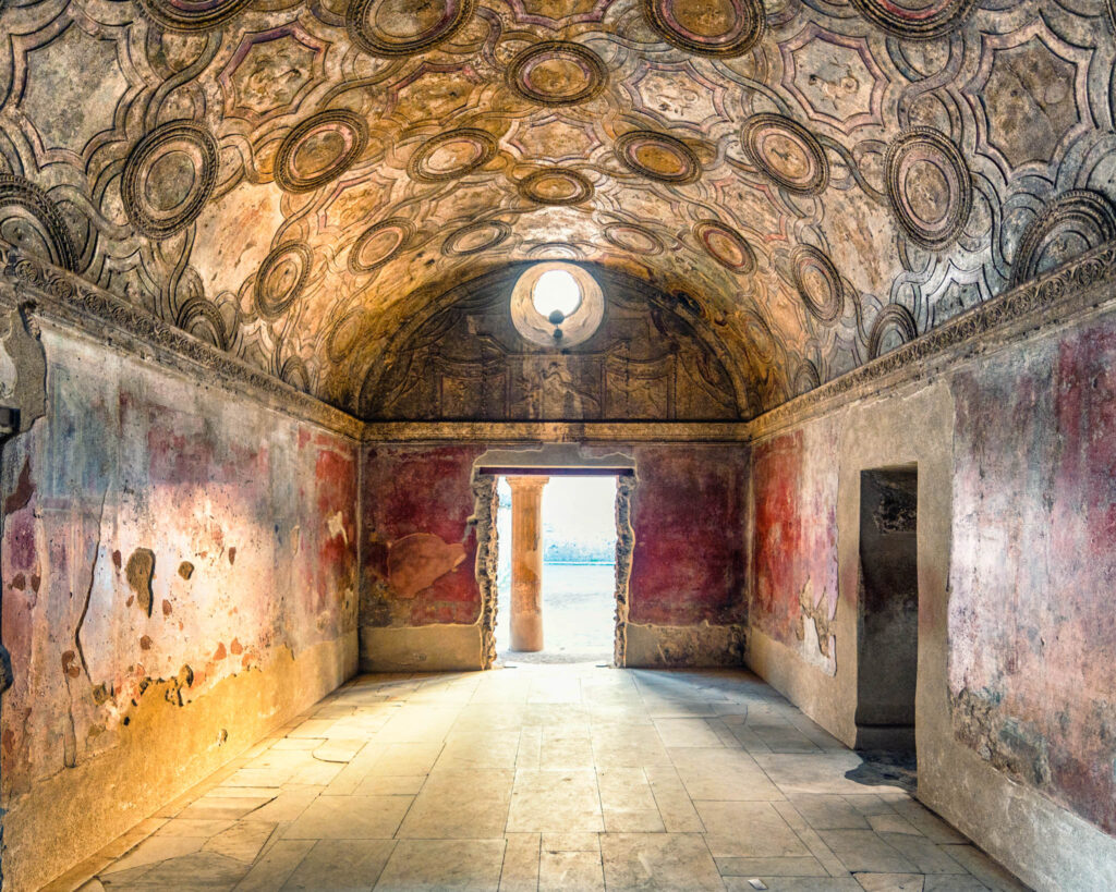 Salle voûtée des Thermes Stabiens à Pompéi avec stucs géométriques, fresques rouges patinées et lumière orangée du coucher du soleil