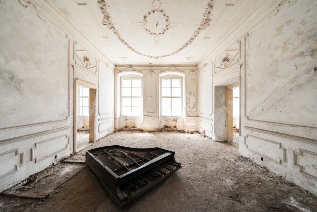 Pièce blanche abandonnée du Palacio Rubato en Pologne, avec un piano au centre, murs décrépis et lumière entrant par les fenêtres.