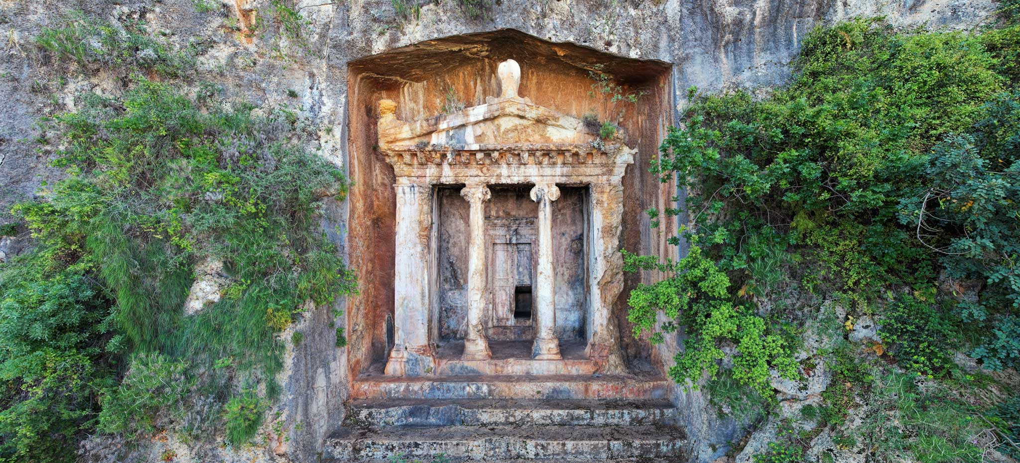 Façade antique du tombeau d'Amyntas taillée dans la roche et partiellement envahie par la nature sauvage à Fethiye en Turquie.
